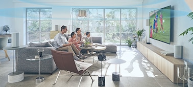 Familia en el sofá viendo el TV con el sistema de Home Theatre HT-A9 en un mueble con Immersive AE activado y ondas de sonido del suelo al techo.