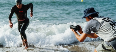 Imagen de uso de un hombre sujetando la cámara para tomar capturas a un triatleta que sale corriendo del mar